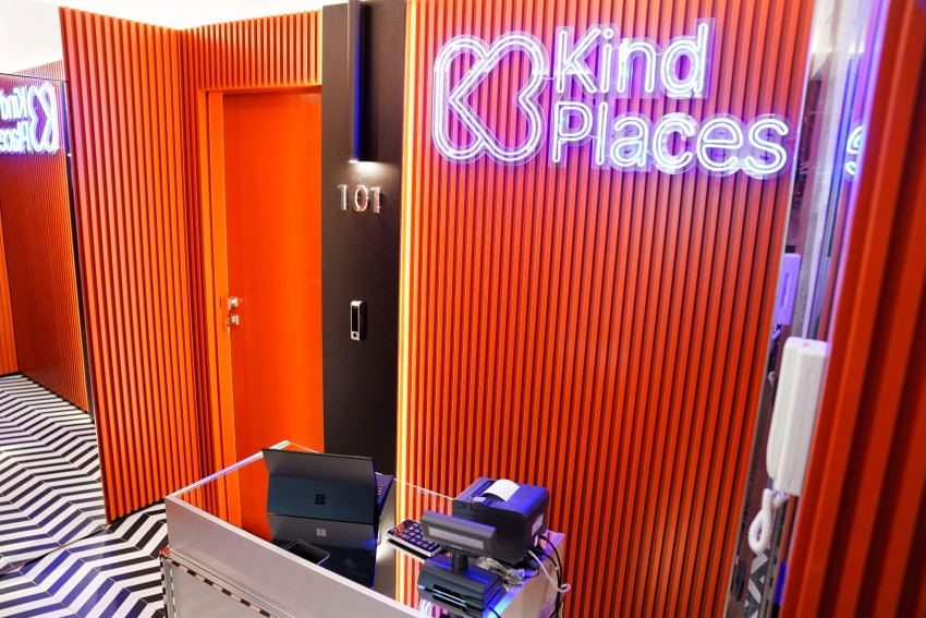 Ingresso di Kind Places con parete in legno arancio e logo al neon